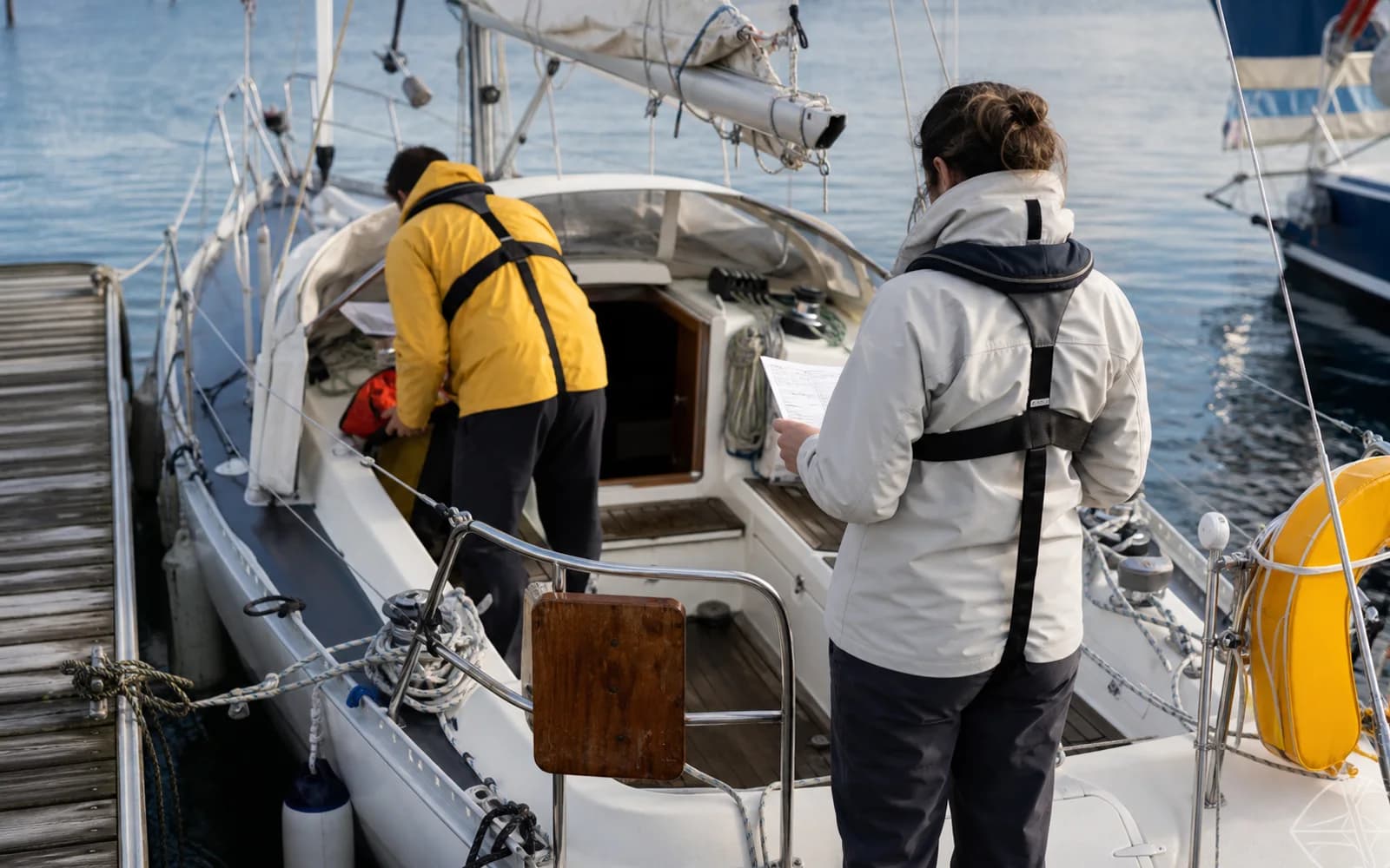 Deux équipiers préparant un voilier au ponton avec une checklist